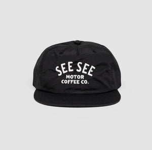 Front shot of black unisex adult surf-style 5-panel hat. Centered text in white reads, See See Moto Coffee Co.