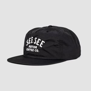 Side angle shot of black unisex adult surf-style 5-panel hat. Centered text in white reads, See See Moto Coffee Co.