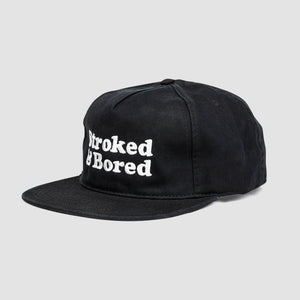 Side angle shot of black cotton unisex 5-panel hat. Centered text in white embroidery reads Stroked & Bored. 