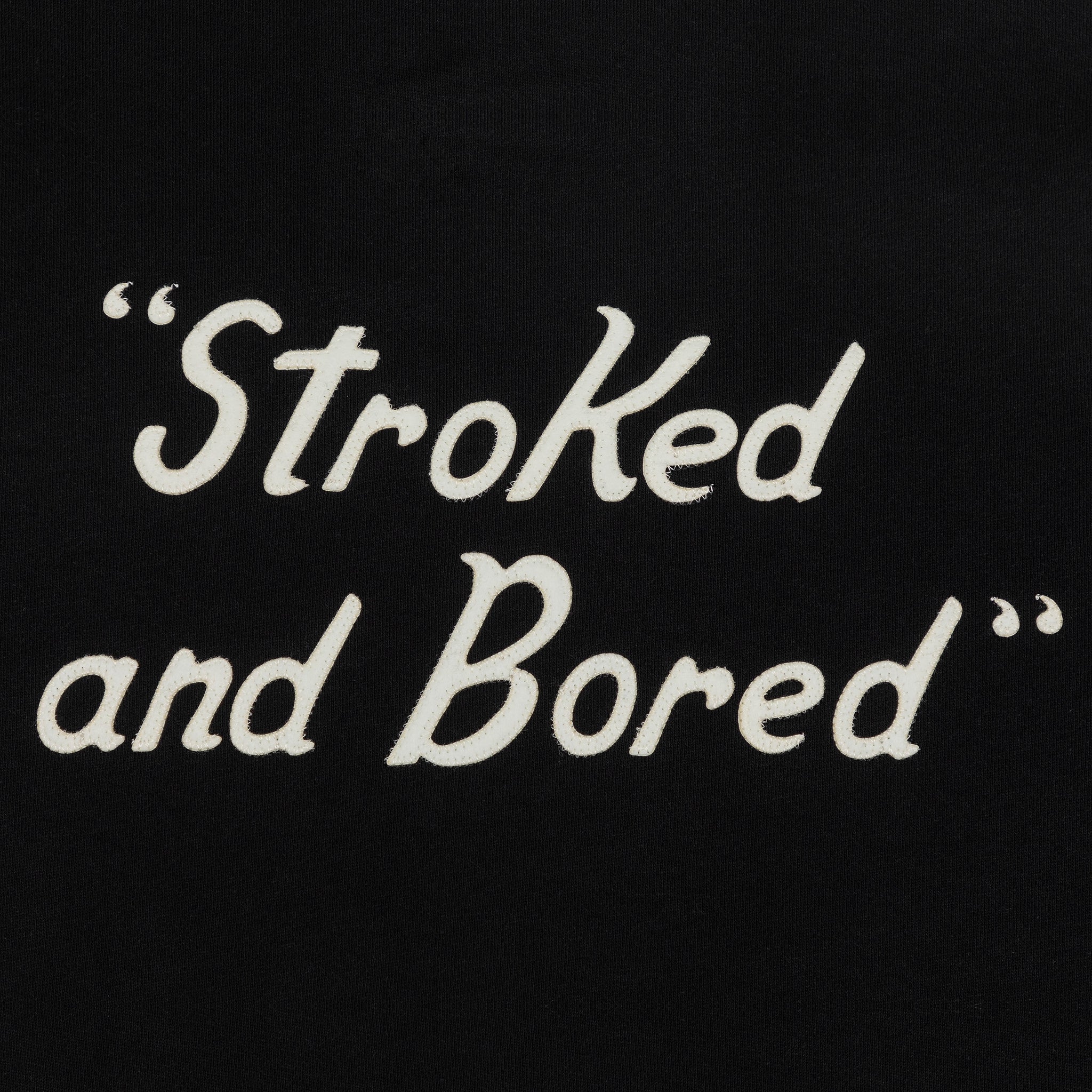 Back detailed shot of embroidered white text saying Stroked and Bored. 